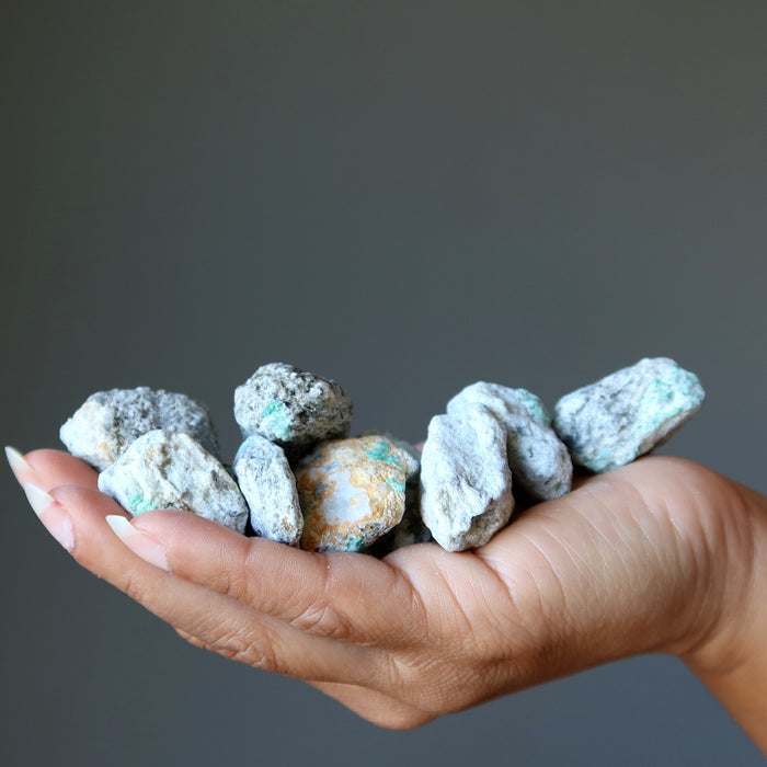 Hand holding a collection of small, rough emerald stones against a dark background