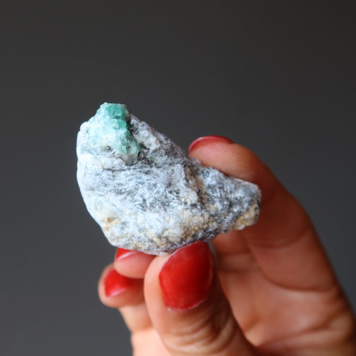 finger tips holding raw Emerald Cluster
