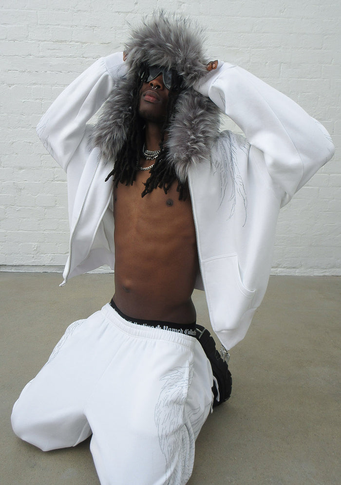 Model wearing a white hoodie with detachable grey fur trim, featuring rhinestone wing design, in a kneeling position.