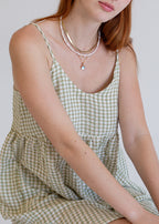 Person wearing a green checkered dress with visible jewelry on a plain background