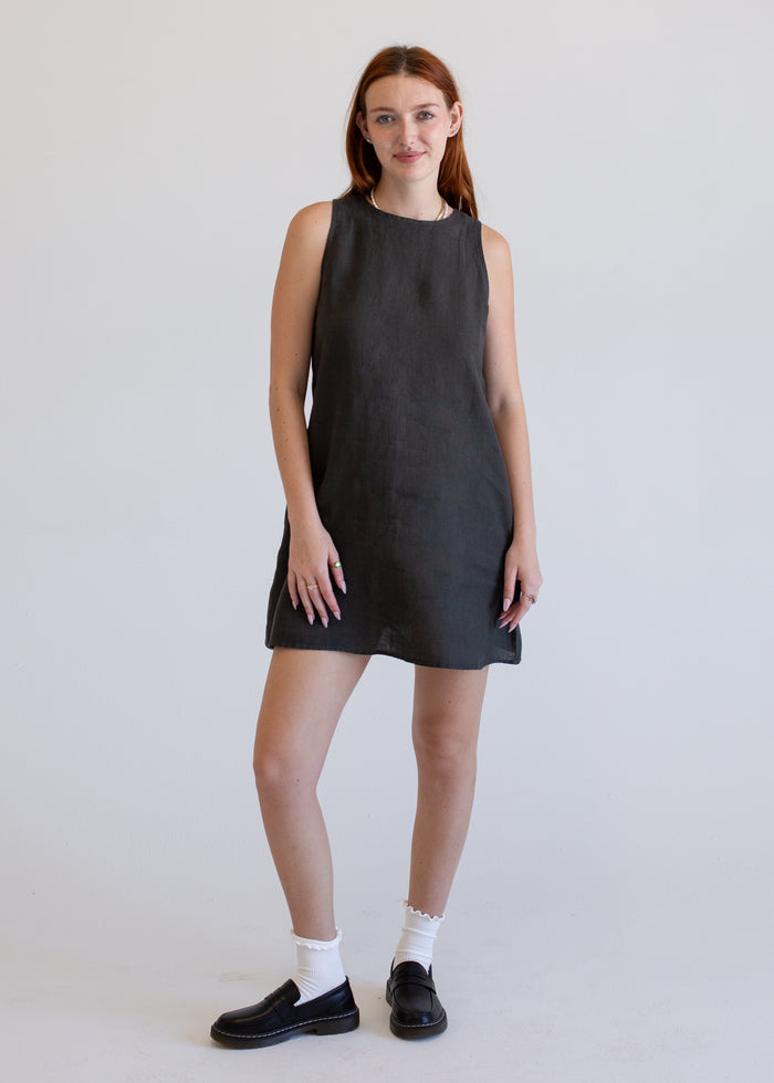 Woman wearing a dark gray sleeveless dress against a plain background